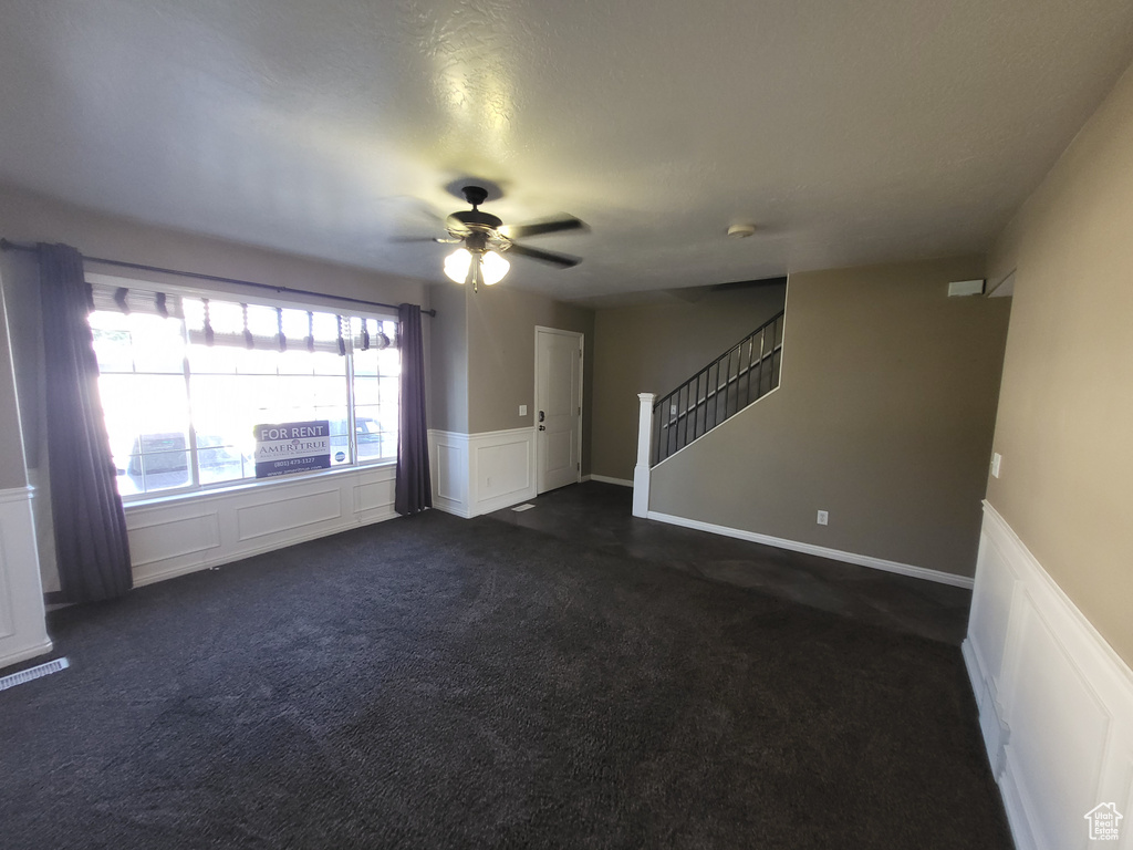 Unfurnished living room featuring ceiling fan and dark carpet