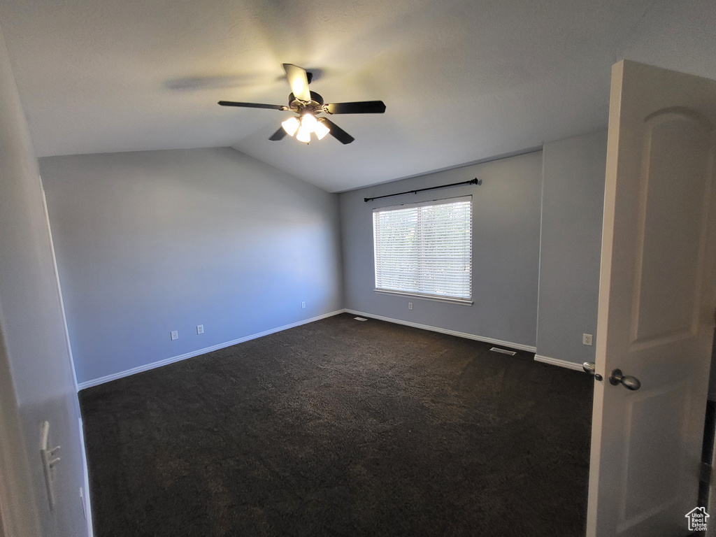 Empty room with dark carpet, vaulted ceiling, and ceiling fan