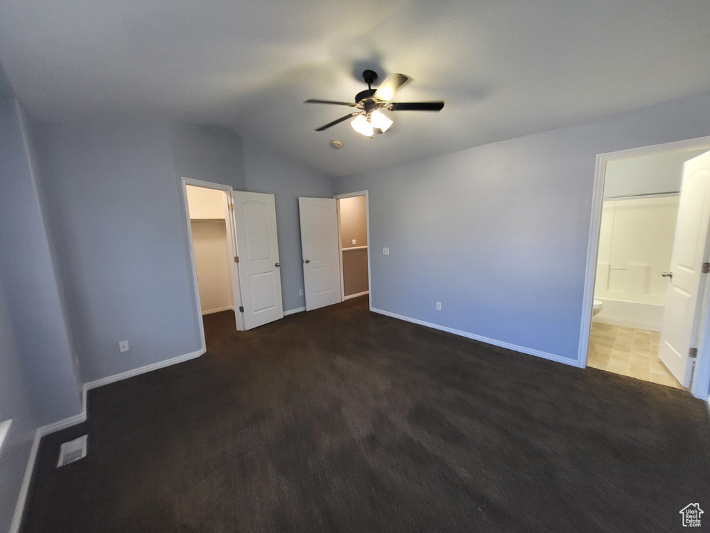 Unfurnished bedroom featuring connected bathroom, dark carpet, ceiling fan, and vaulted ceiling