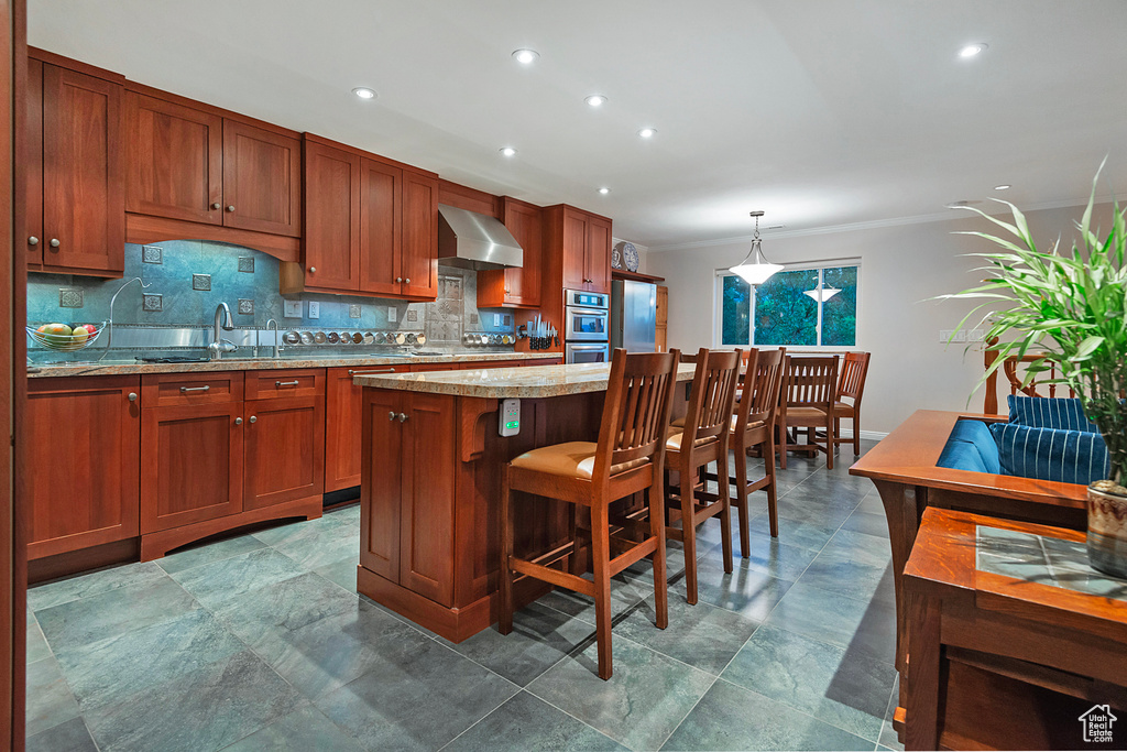 Kitchen featuring dark tile flooring, hanging light fixtures, wall chimney exhaust hood, tasteful backsplash, and a center island
