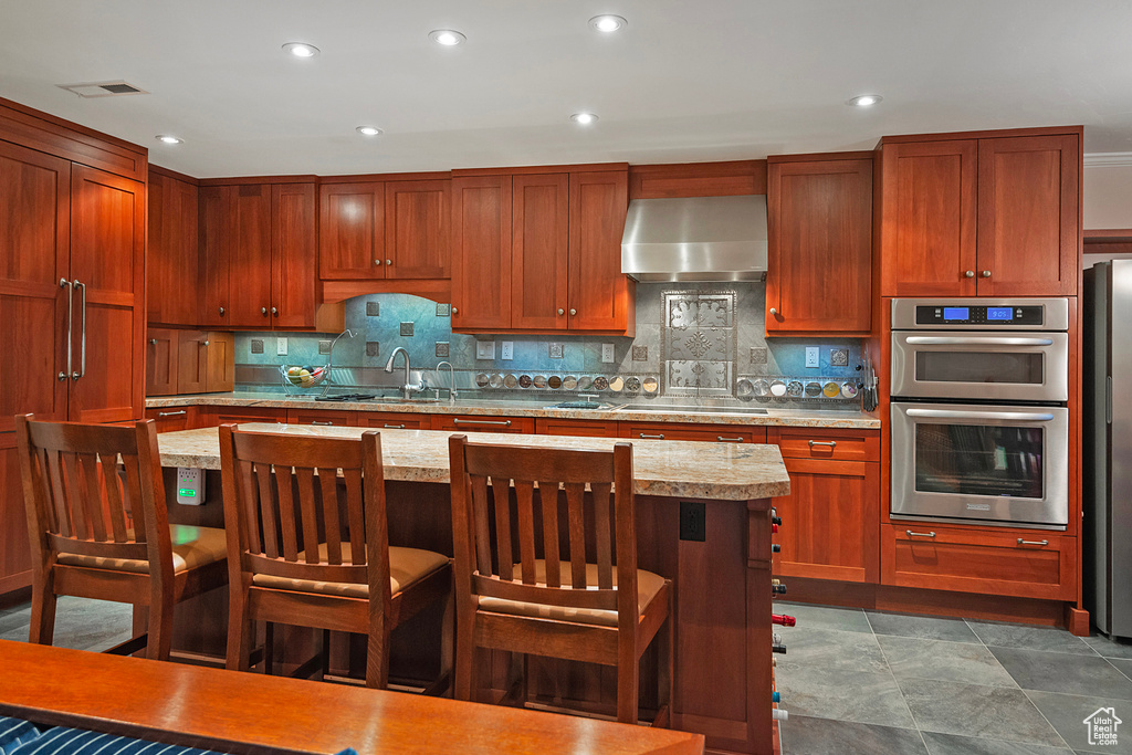 Kitchen with a kitchen bar, wall chimney exhaust hood, stainless steel appliances, and backsplash