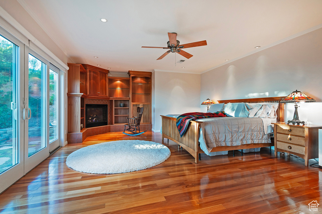 Bedroom featuring ceiling fan, a tile fireplace, crown molding, hardwood / wood-style floors, and access to outside