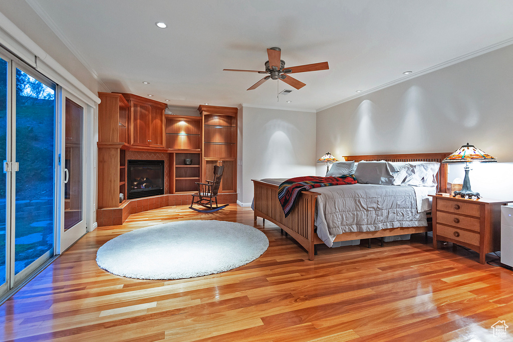 Bedroom featuring ceiling fan, light wood-type flooring, access to outside, a tile fireplace, and crown molding