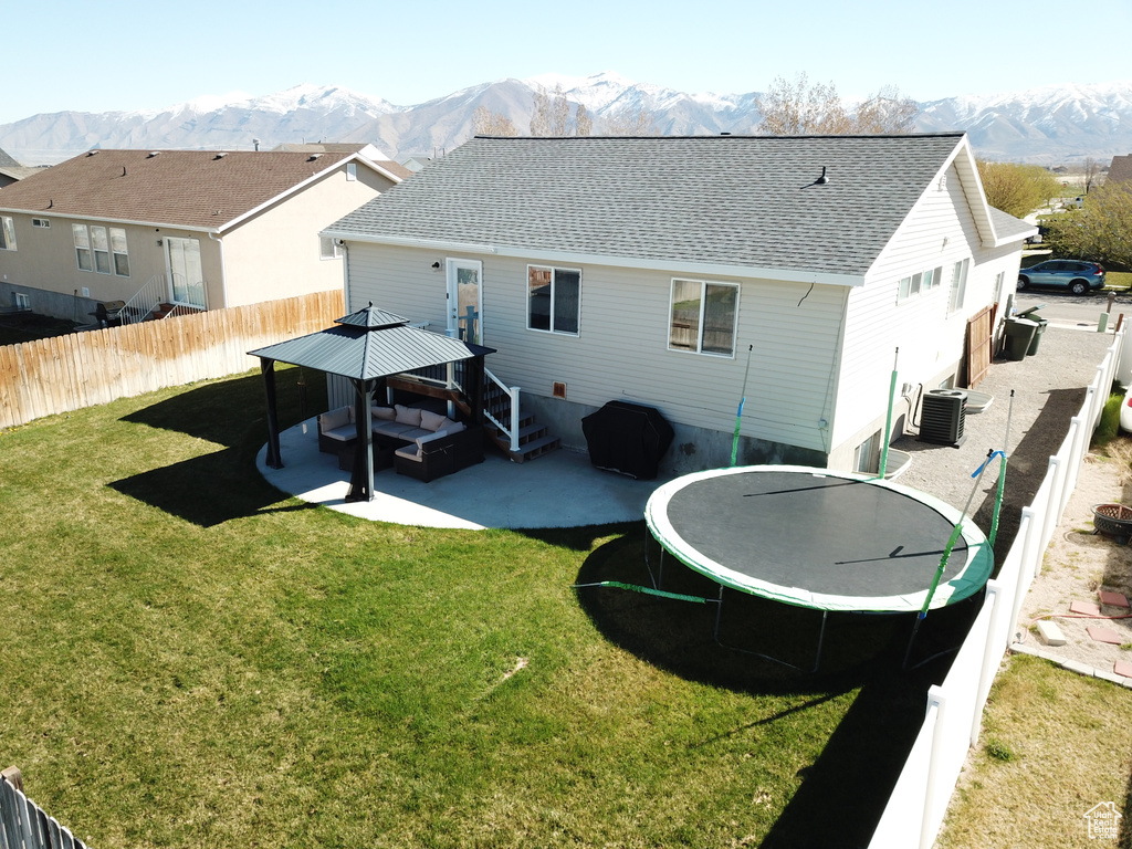 Rear view of house featuring a lawn, a mountain view, a trampoline, and central AC unit