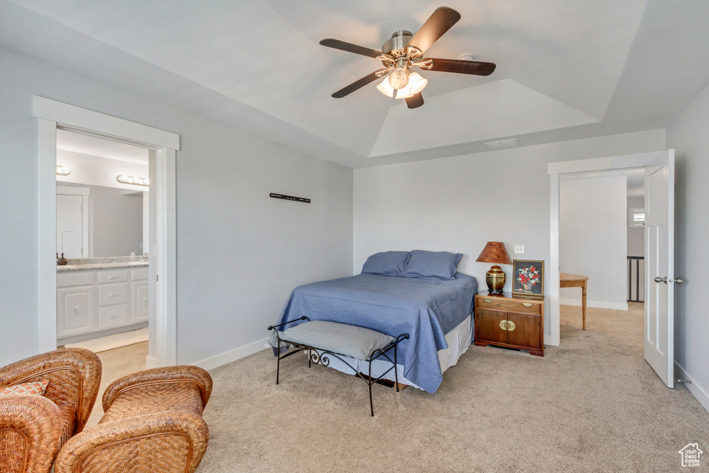 Bedroom with light colored carpet, a tray ceiling, ensuite bath, and ceiling fan