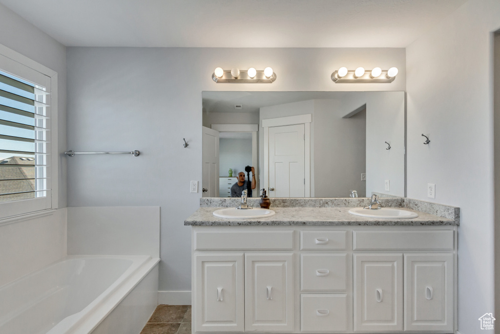 Bathroom with large vanity, dual sinks, tile floors, and a bath