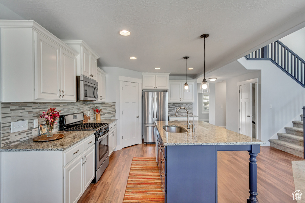 Kitchen featuring sink, light wood-type flooring, stainless steel appliances, white cabinets, and pendant lighting
