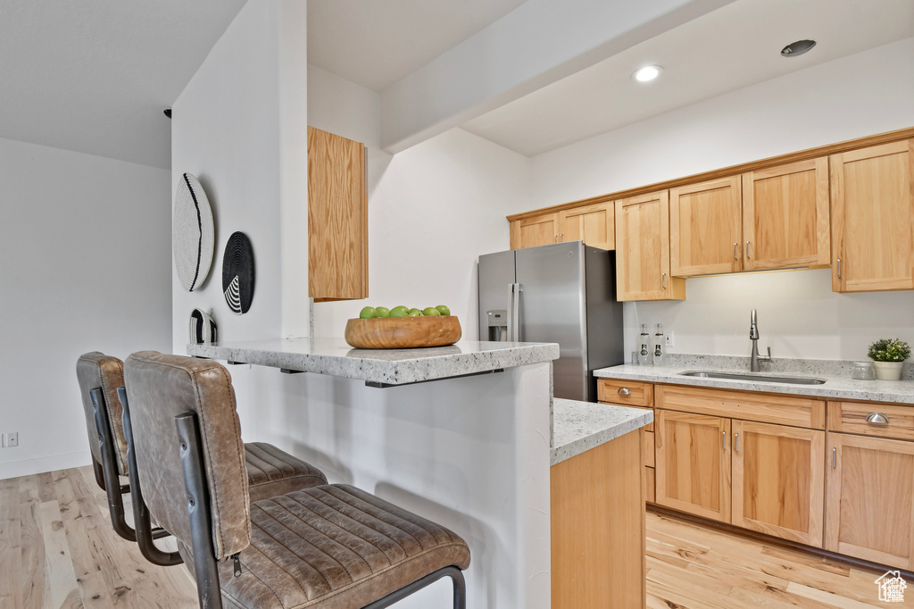 Kitchen featuring a kitchen breakfast bar, light stone countertops, light hardwood / wood-style floors, and sink