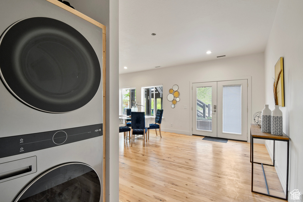 Clothes washing area featuring light hardwood / wood-style floors, french doors, and stacked washer and dryer