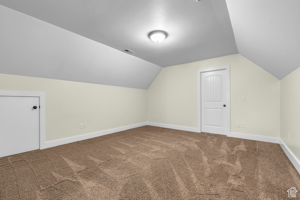 Additional living space with dark carpet and vaulted ceiling