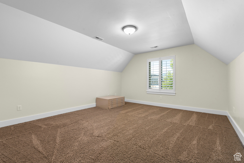 Additional living space with vaulted ceiling and dark colored carpet