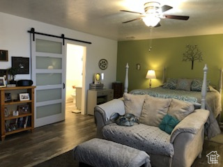 Bedroom featuring a barn door, dark wood-type flooring, ceiling fan, and ensuite bathroom
