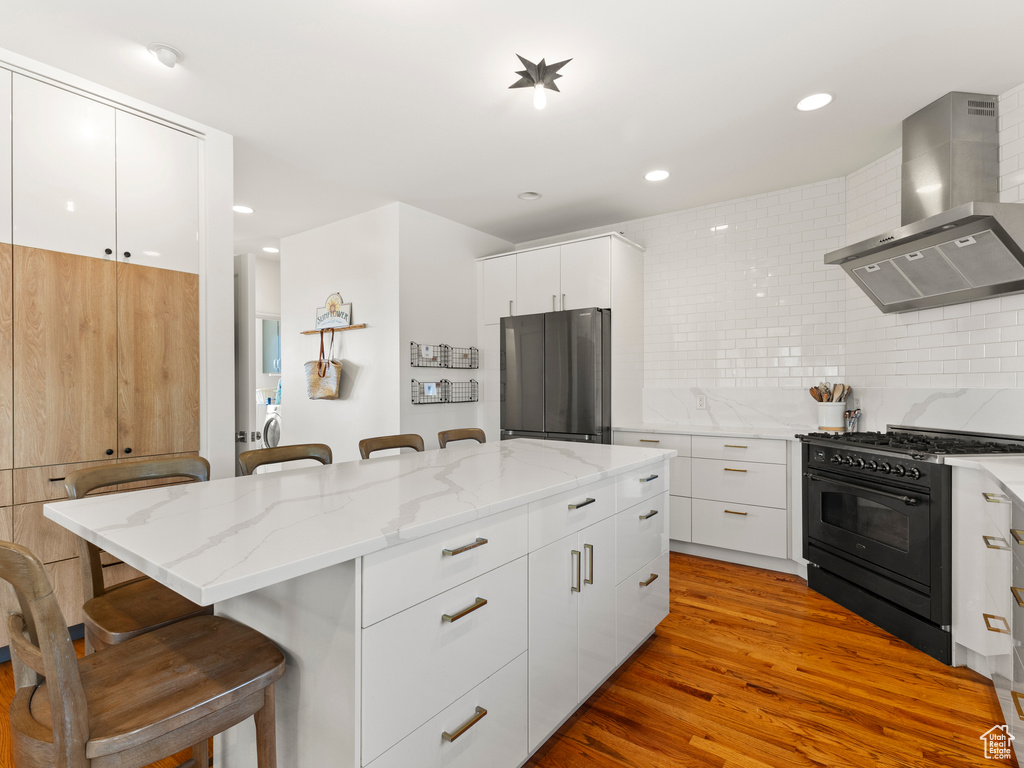 Kitchen with double oven range, backsplash, wall chimney exhaust hood, and a breakfast bar area