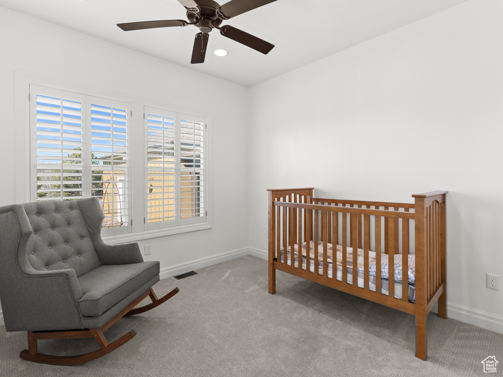 Carpeted bedroom with a crib and ceiling fan