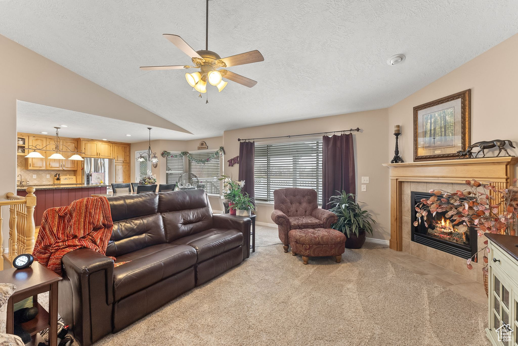 Living room featuring light colored carpet, ceiling fan, a textured ceiling, a fireplace, and lofted ceiling