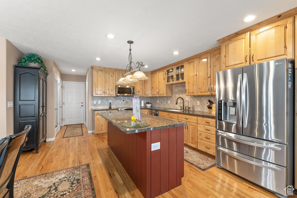 Kitchen featuring a kitchen island, appliances with stainless steel finishes, backsplash, light hardwood / wood-style floors, and decorative light fixtures