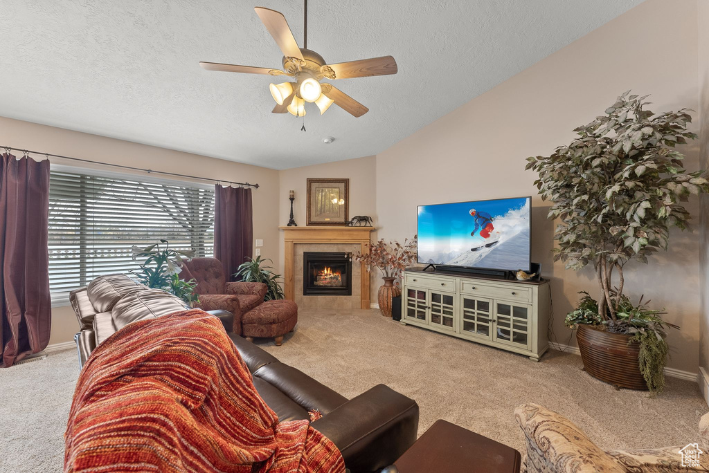 Carpeted living room with ceiling fan, a textured ceiling, a tile fireplace, and vaulted ceiling