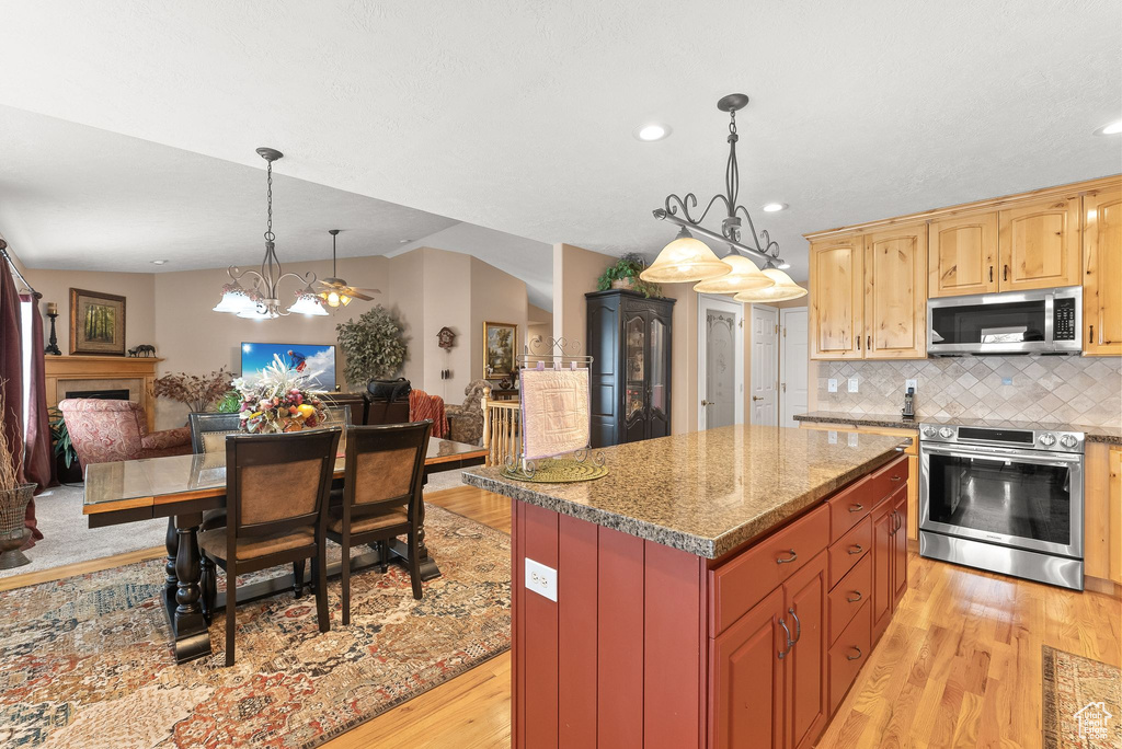 Kitchen with an inviting chandelier, a kitchen island, stainless steel appliances, light wood-type flooring, and pendant lighting