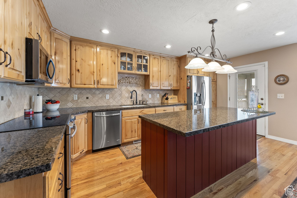 Kitchen with a center island, appliances with stainless steel finishes, light wood-type flooring, and sink