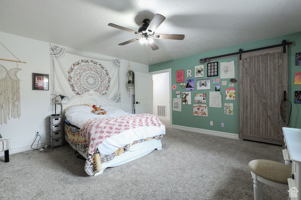 Carpeted bedroom with a barn door, ceiling fan, and a textured ceiling