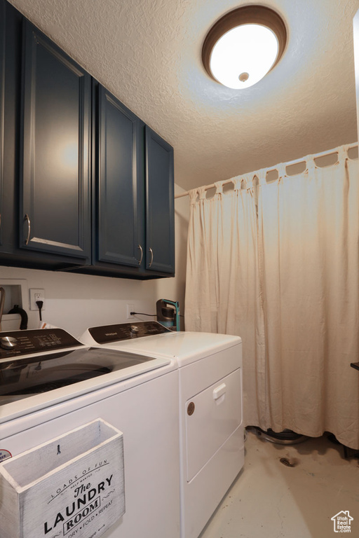 Clothes washing area with washing machine and clothes dryer, cabinets, and a textured ceiling