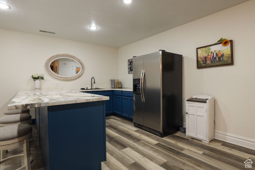 Kitchen with hardwood / wood-style flooring, a breakfast bar, blue cabinets, stainless steel refrigerator with ice dispenser, and sink