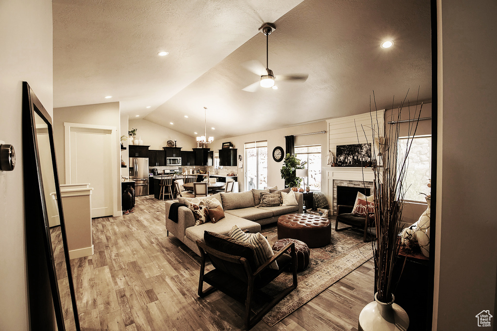 Living room featuring light hardwood / wood-style floors, ceiling fan with notable chandelier, and vaulted ceiling