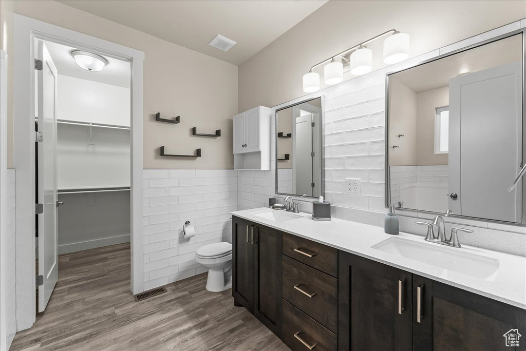 Bathroom featuring double sink, tile walls, toilet, large vanity, and hardwood / wood-style flooring