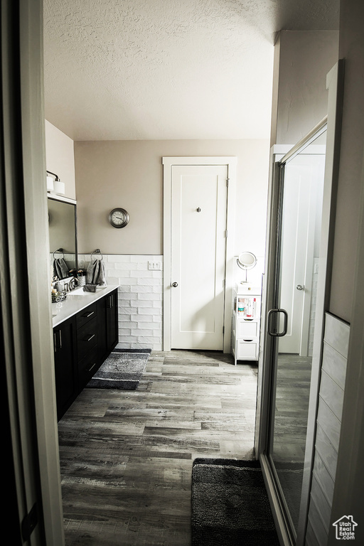Bathroom featuring a textured ceiling, a shower with door, wood-type flooring, and vanity