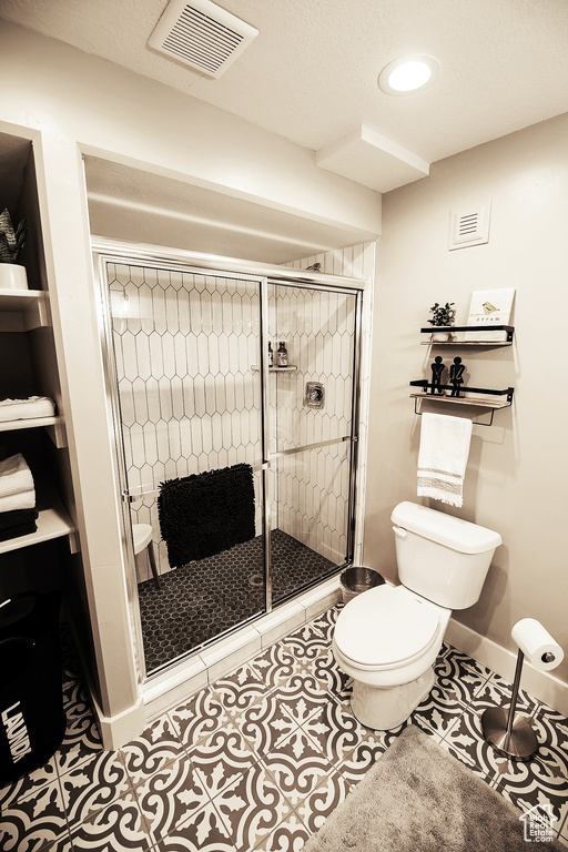 Bathroom with toilet, a textured ceiling, tile floors, and a shower with shower door