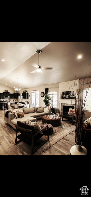 Living room featuring wood-type flooring, ceiling fan with notable chandelier, a fireplace, and lofted ceiling