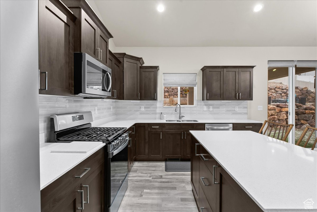Kitchen with sink, appliances with stainless steel finishes, light hardwood / wood-style flooring, backsplash, and dark brown cabinetry