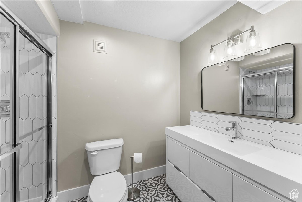 Bathroom with a shower with door, tile flooring, toilet, tasteful backsplash, and large vanity