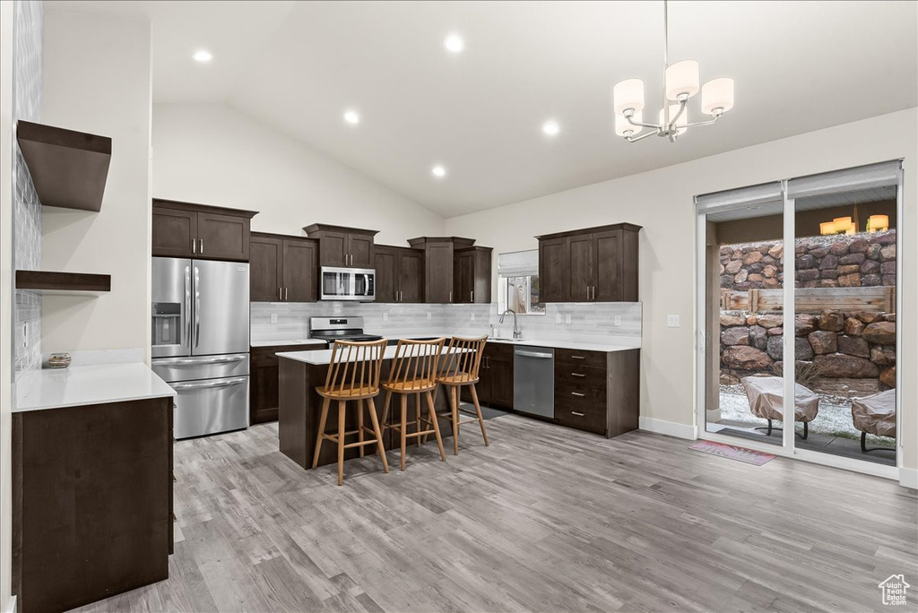Kitchen featuring tasteful backsplash, light hardwood / wood-style floors, appliances with stainless steel finishes, and a chandelier