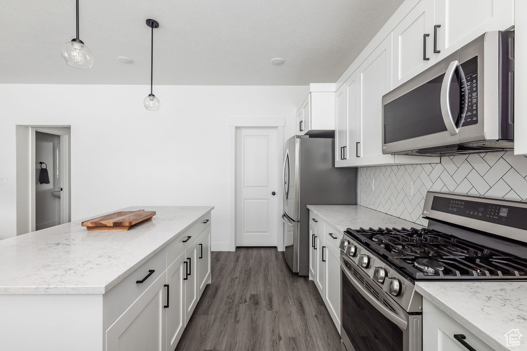 Kitchen with backsplash, stainless steel appliances, white cabinets, dark hardwood / wood-style flooring, and pendant lighting
