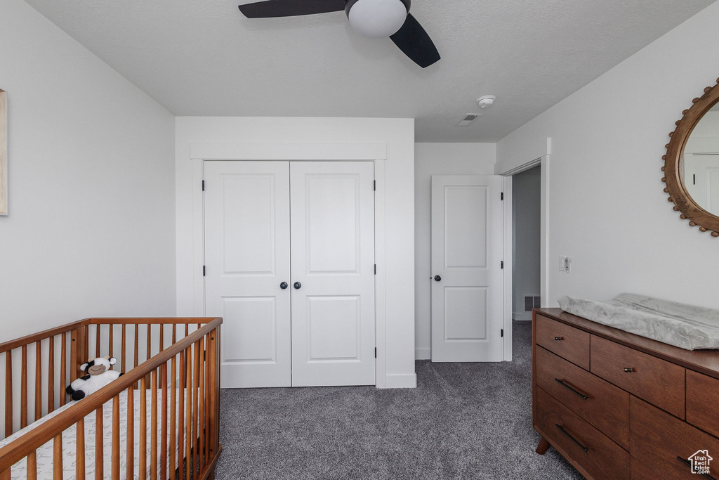 Carpeted bedroom featuring a closet, a nursery area, and ceiling fan