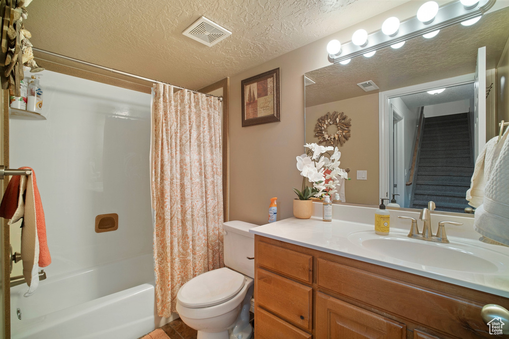 Full bathroom featuring oversized vanity, a textured ceiling, toilet, and shower / bath combo