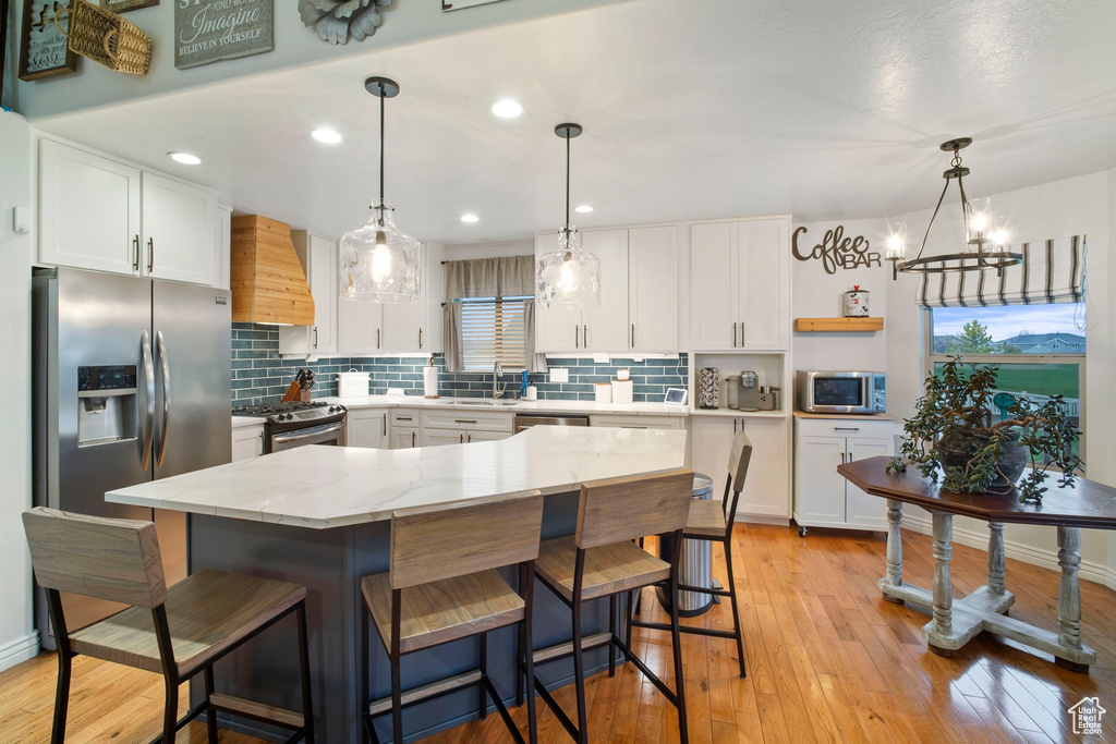Kitchen with pendant lighting, light hardwood / wood-style floors, white cabinets, and premium range hood