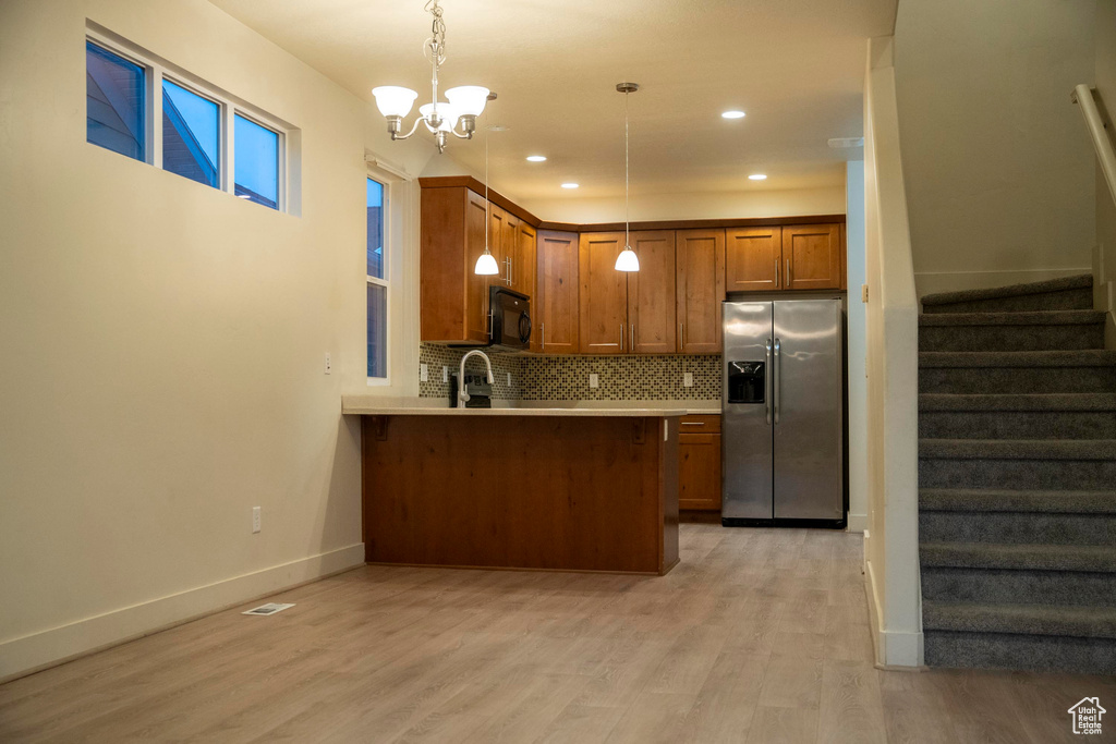 Kitchen with an inviting chandelier, hanging light fixtures, stainless steel fridge, and light hardwood / wood-style flooring