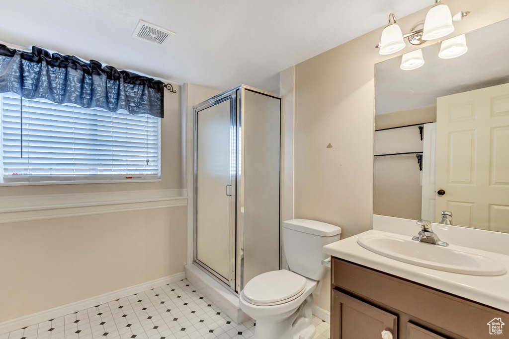Bathroom featuring a notable chandelier, tile floors, vanity with extensive cabinet space, toilet, and a shower with shower door