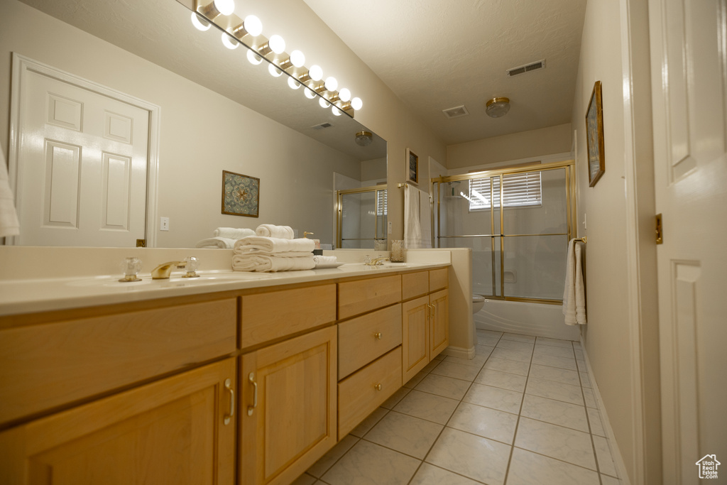 Bathroom with double sink vanity, tile flooring, and bath / shower combo with glass door
