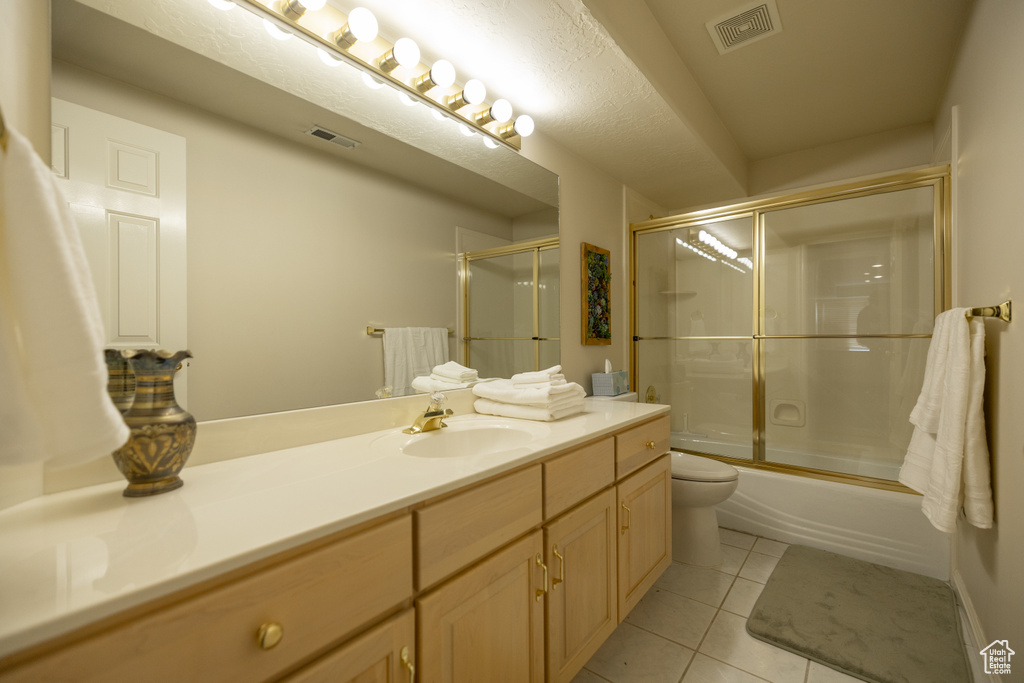 Full bathroom with enclosed tub / shower combo, toilet, tile floors, and vanity