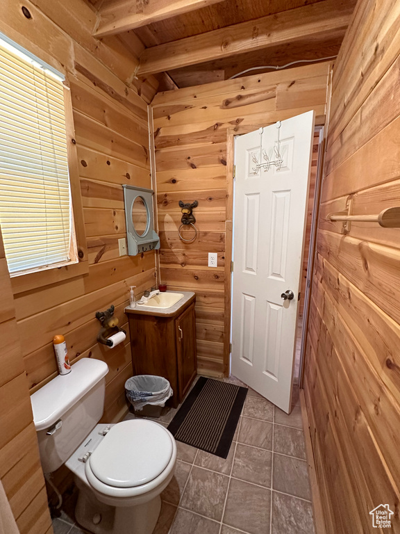 Bathroom featuring toilet, tile floors, wood walls, beam ceiling, and vanity