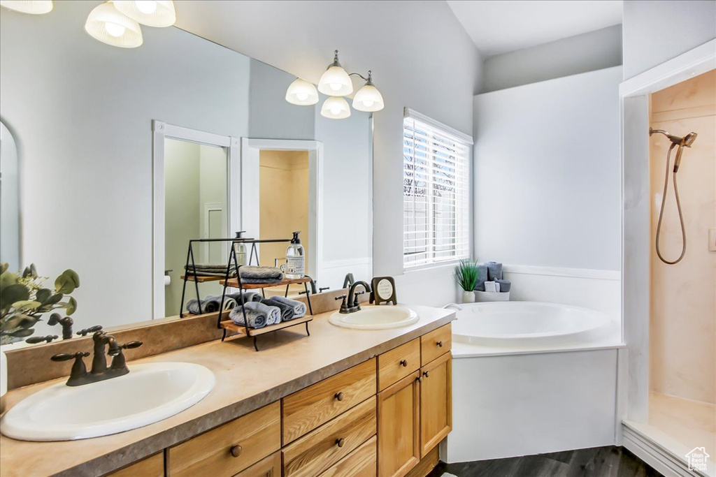 Bathroom with shower with separate bathtub, hardwood / wood-style floors, vanity with extensive cabinet space, and double sink