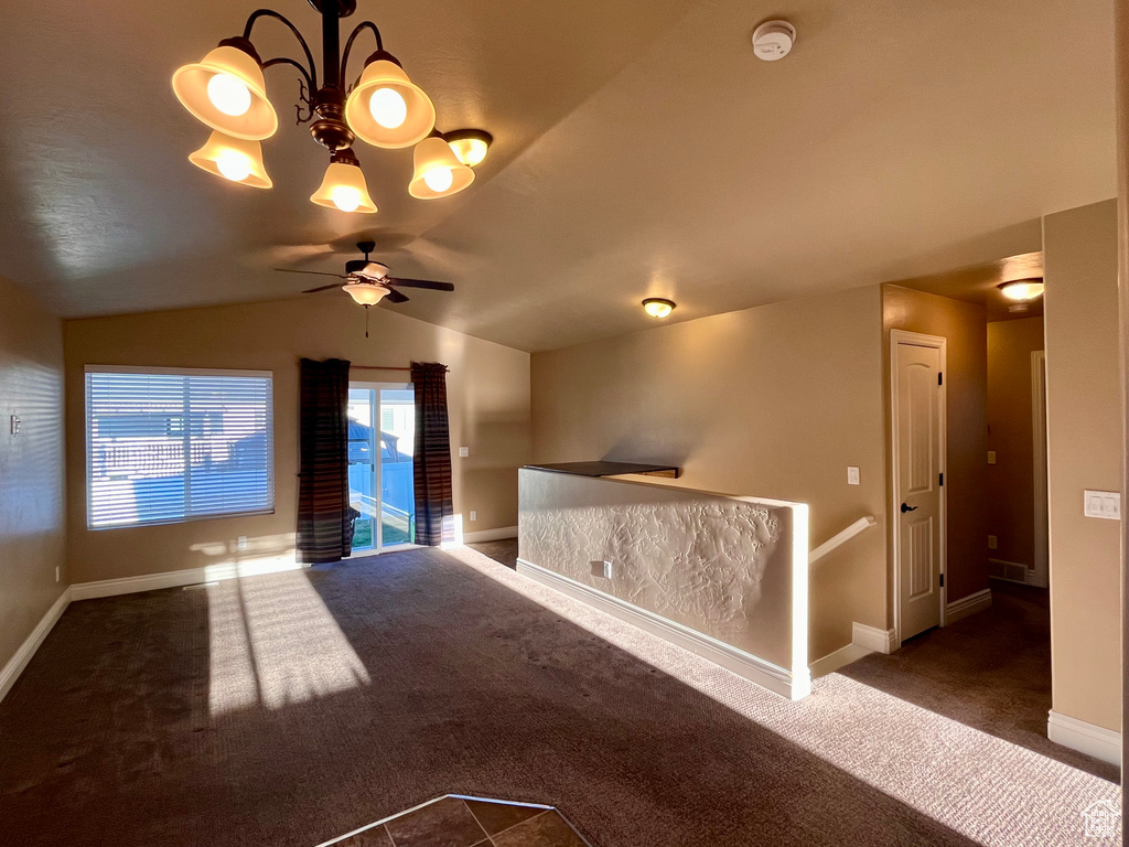 Carpeted empty room with lofted ceiling and ceiling fan with notable chandelier