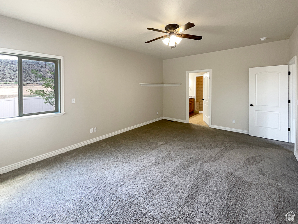 Unfurnished bedroom featuring dark carpet, connected bathroom, and ceiling fan