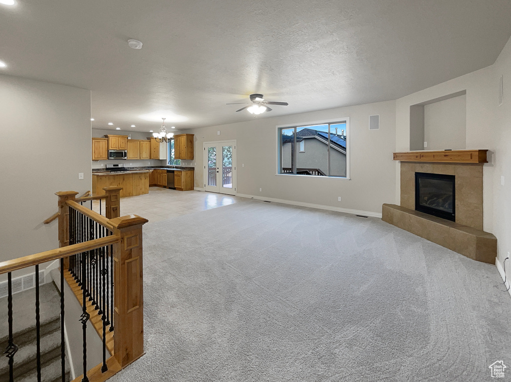 Unfurnished living room featuring a chandelier, a fireplace, ceiling fan, recessed lighting, and light carpet