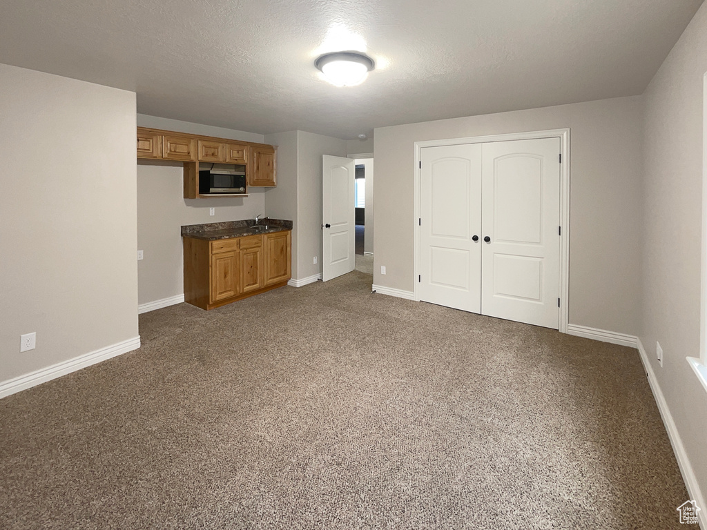 Kitchen with dark countertops, brown cabinets, carpet, and stainless steel microwave