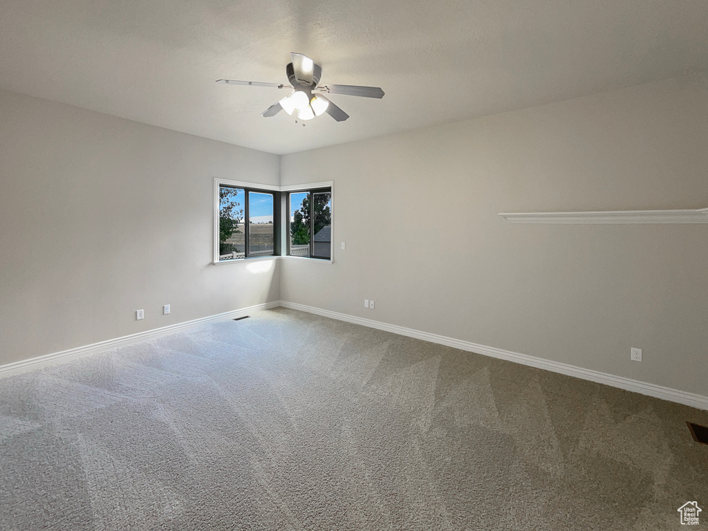 Carpeted empty room featuring ceiling fan and baseboards