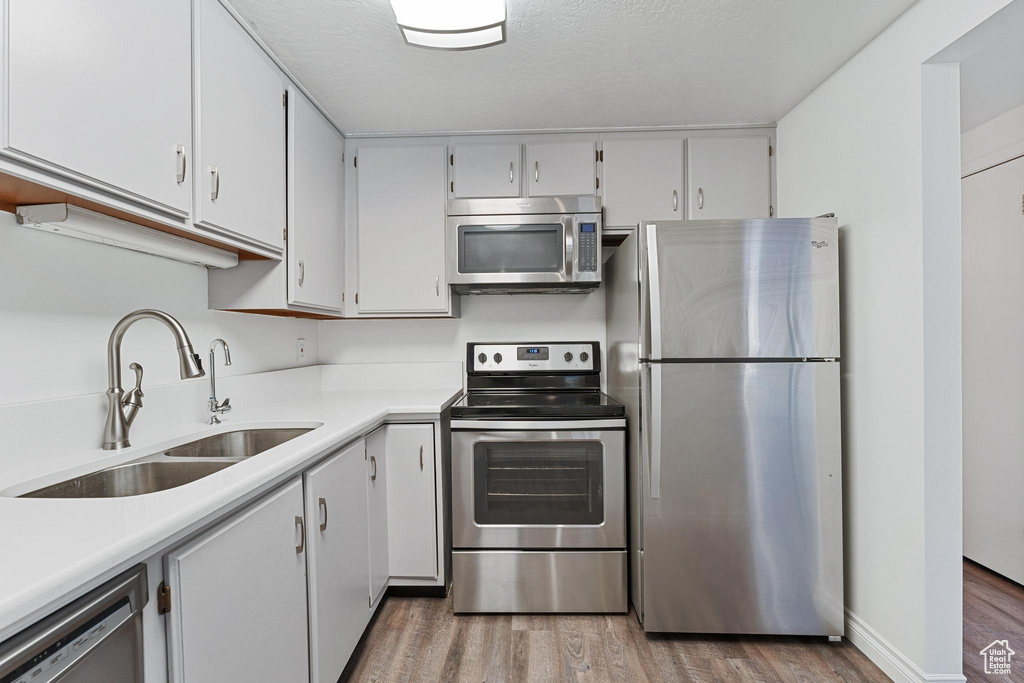 Kitchen with white cabinetry, hardwood / wood-style floors, stainless steel appliances, and sink